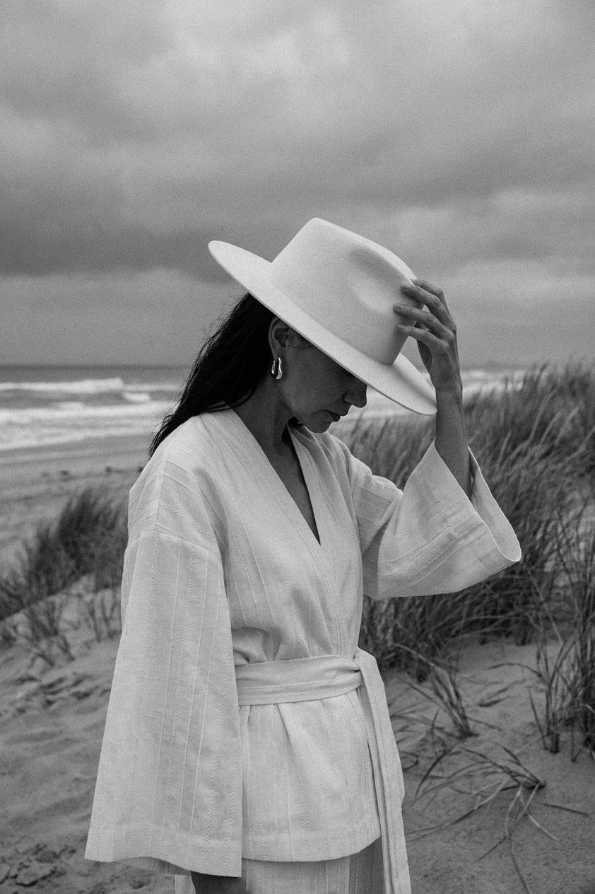 Woman in a white robe and hat on a beach with a cloudy sky